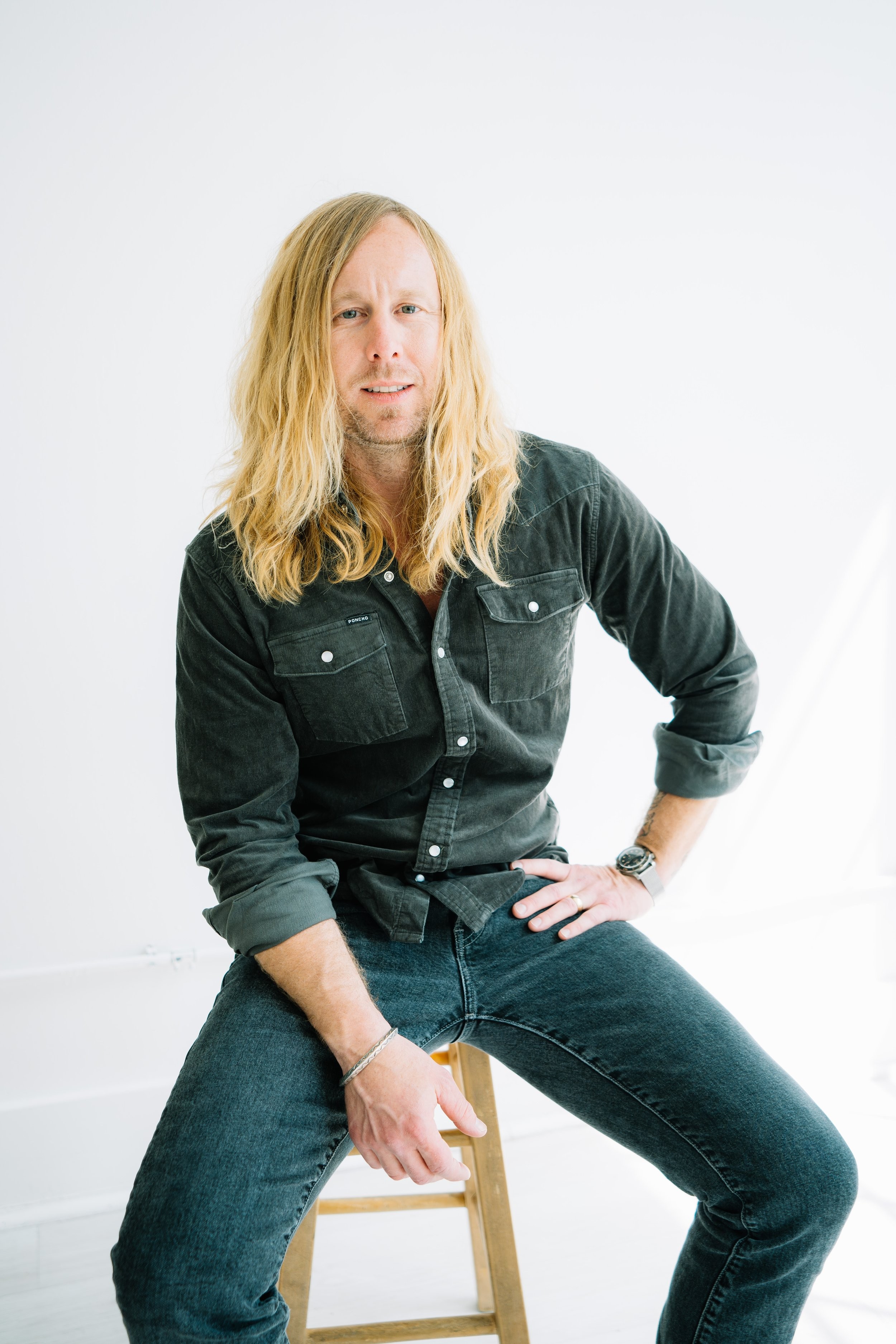 Jamey Ice seated on a stool in a white studio.