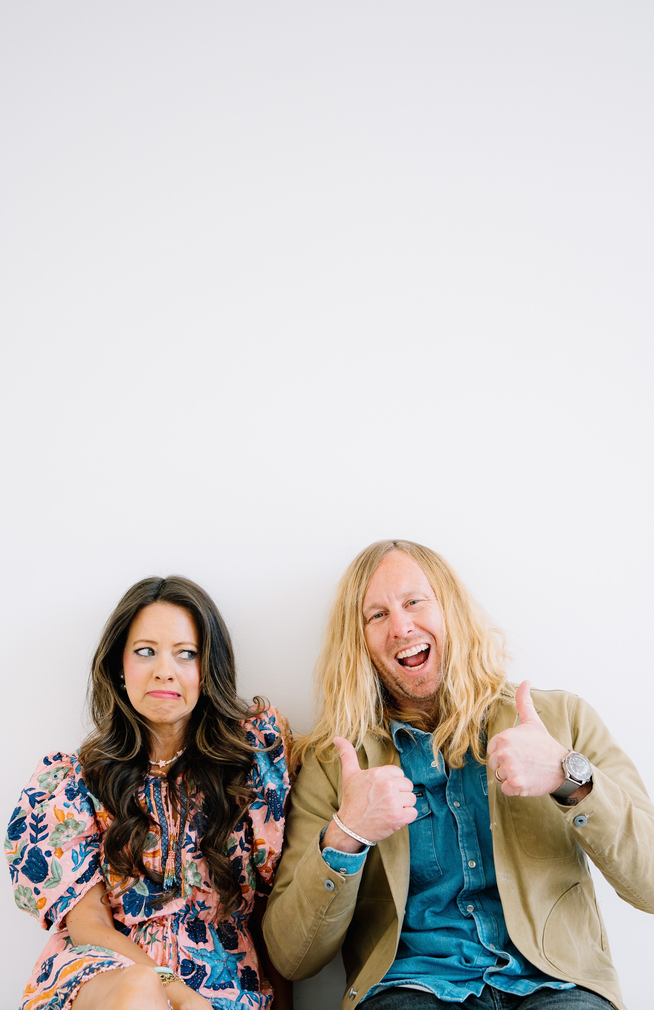 Jamey and Melissa Ice against a white wall, he with two thumbs up, she unconvinced