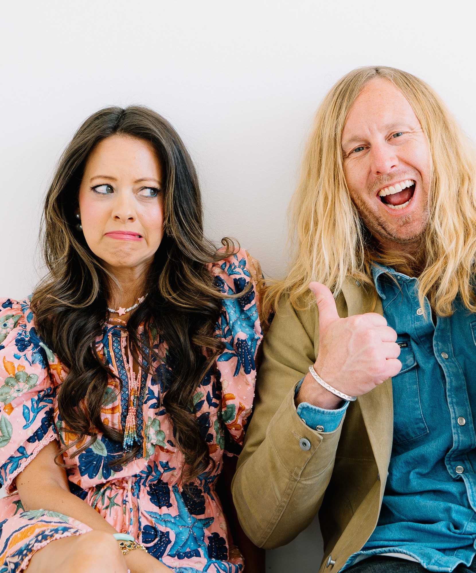 Jamey and Melissa Ice against a white wall, he with two thumbs up, she unconvinced
