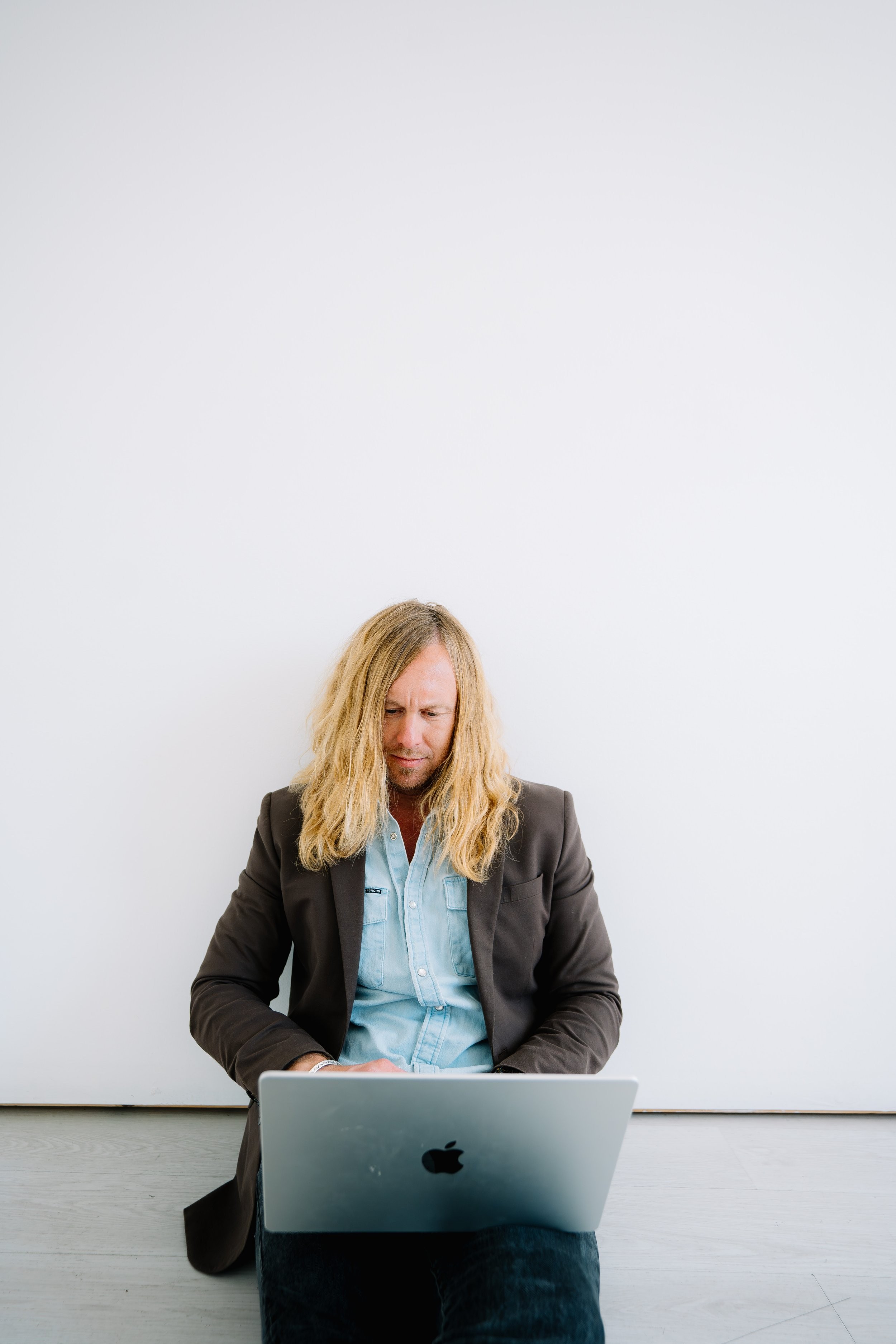 Jamey Ice seated on the floor with a laptop, in a white studio