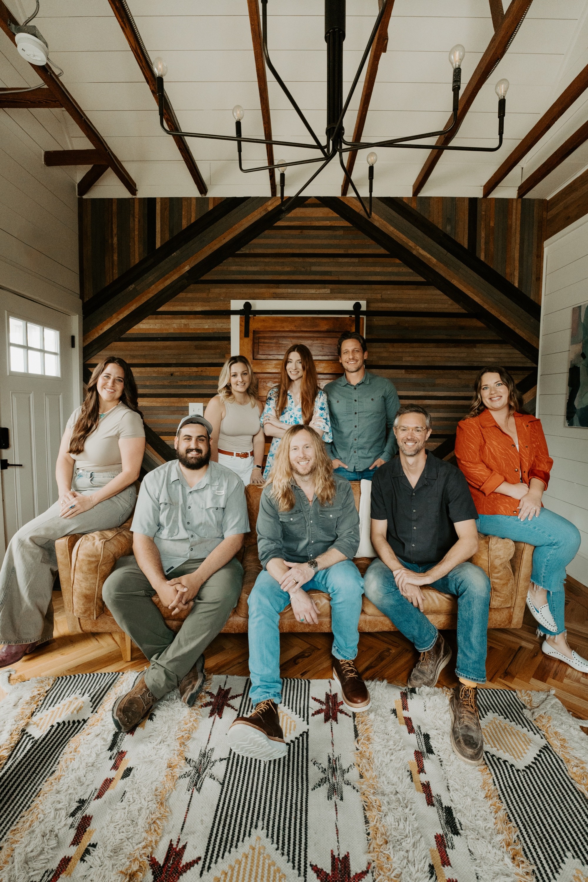 Jamey Ice in the middle of a sofa with seven of the 6th Ave Homes construction team around him, under the beams of a finished build.