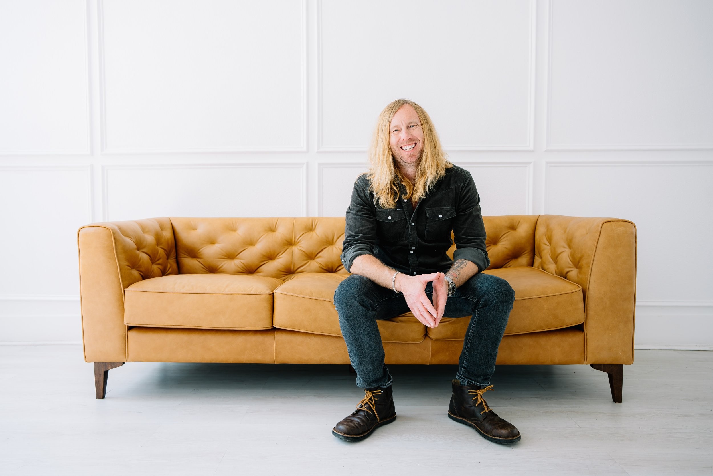 Jamey Ice seated on a leather couch in a white room.