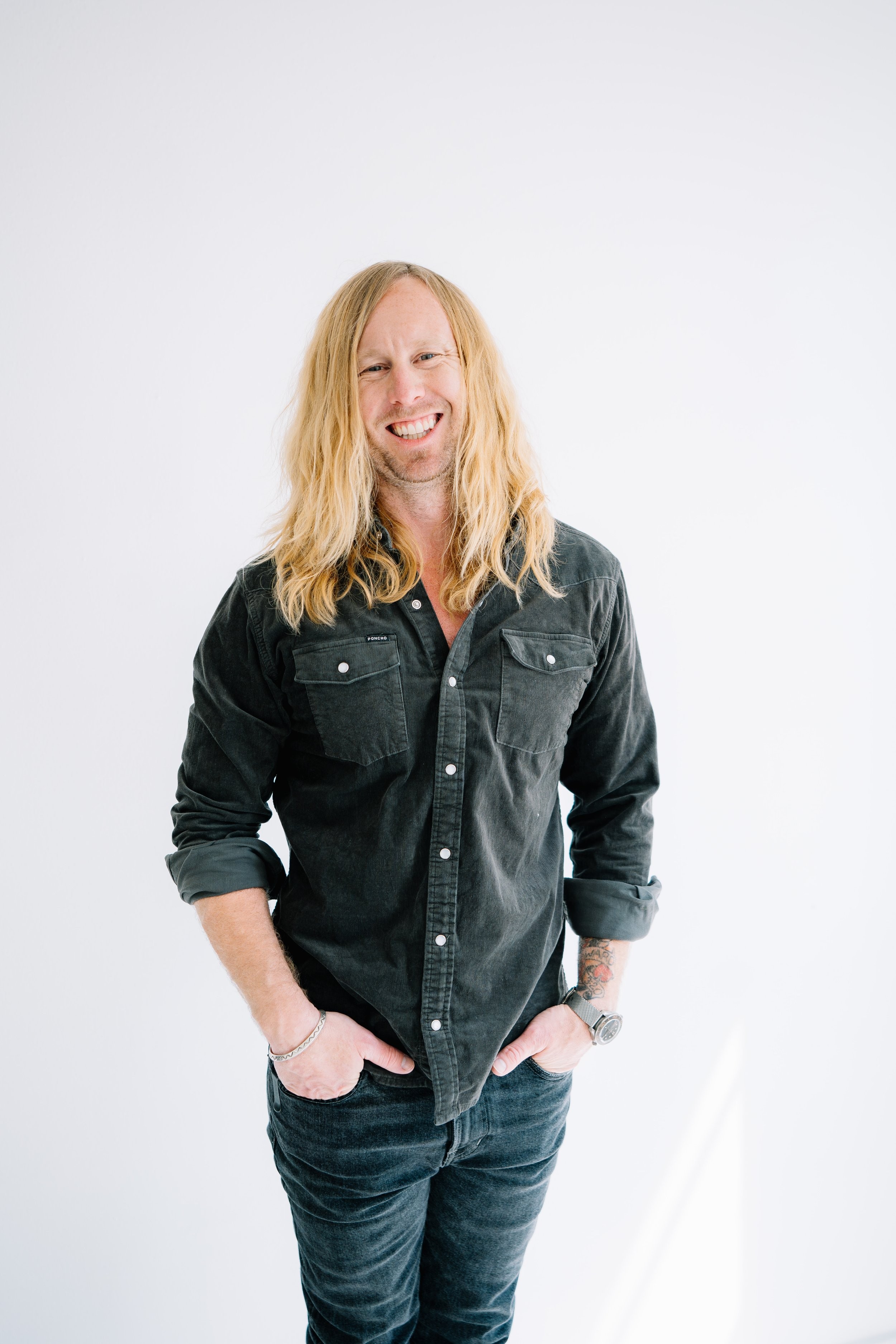 Jamey Ice standing with his hands in his pockets, in a white studio