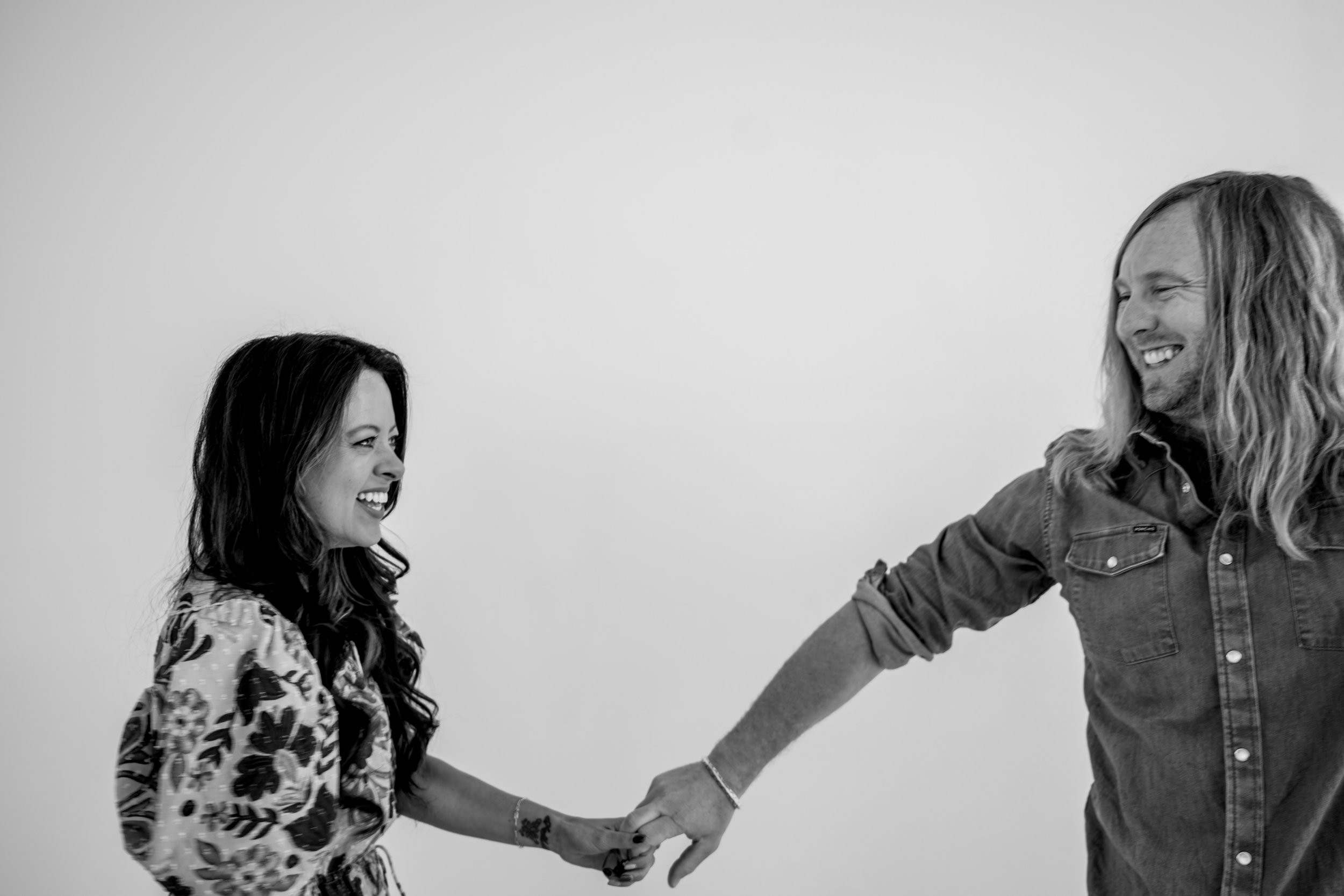 Jamey and Melissa Ice laughing, holding hands at arm's length, in black and white