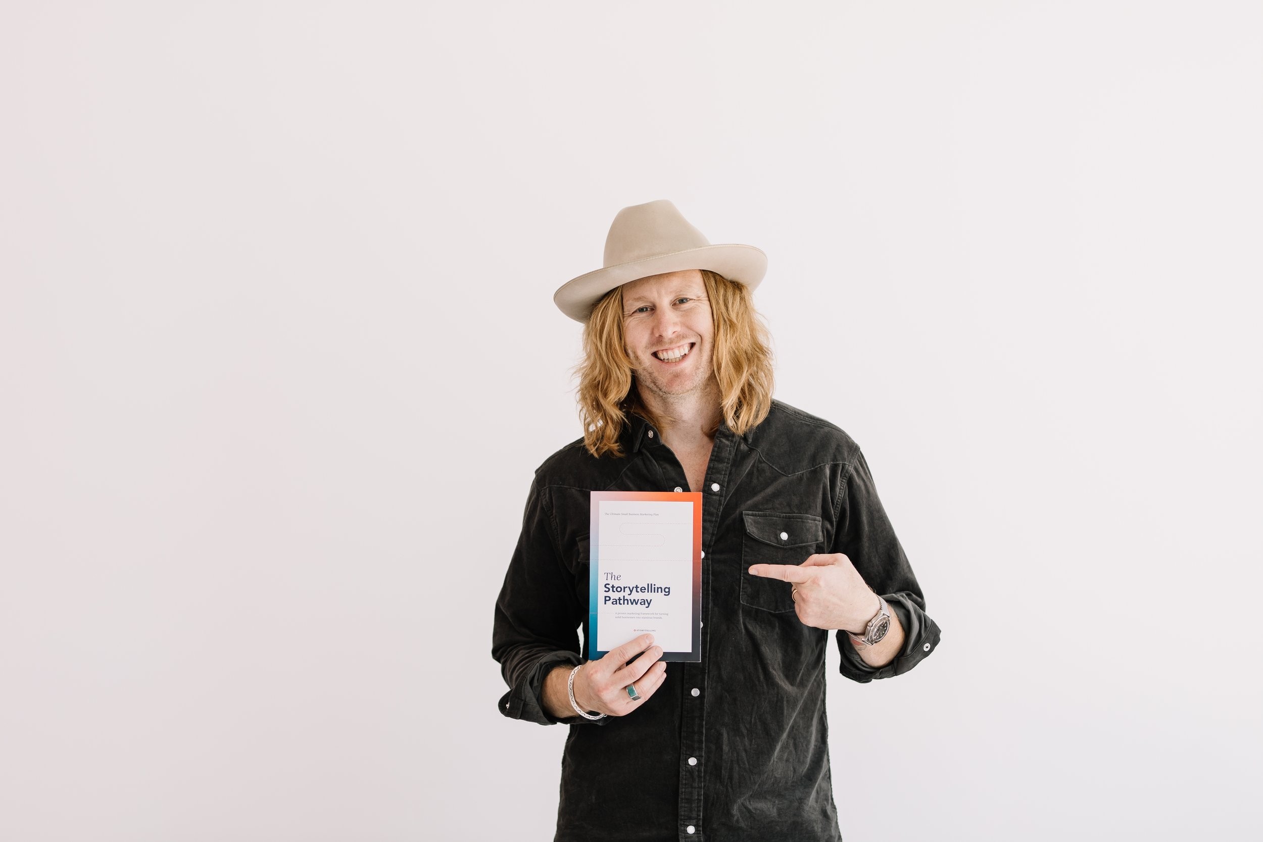 Jamey Ice pointing to a copy of The Storytelling Pathway against a white wall.