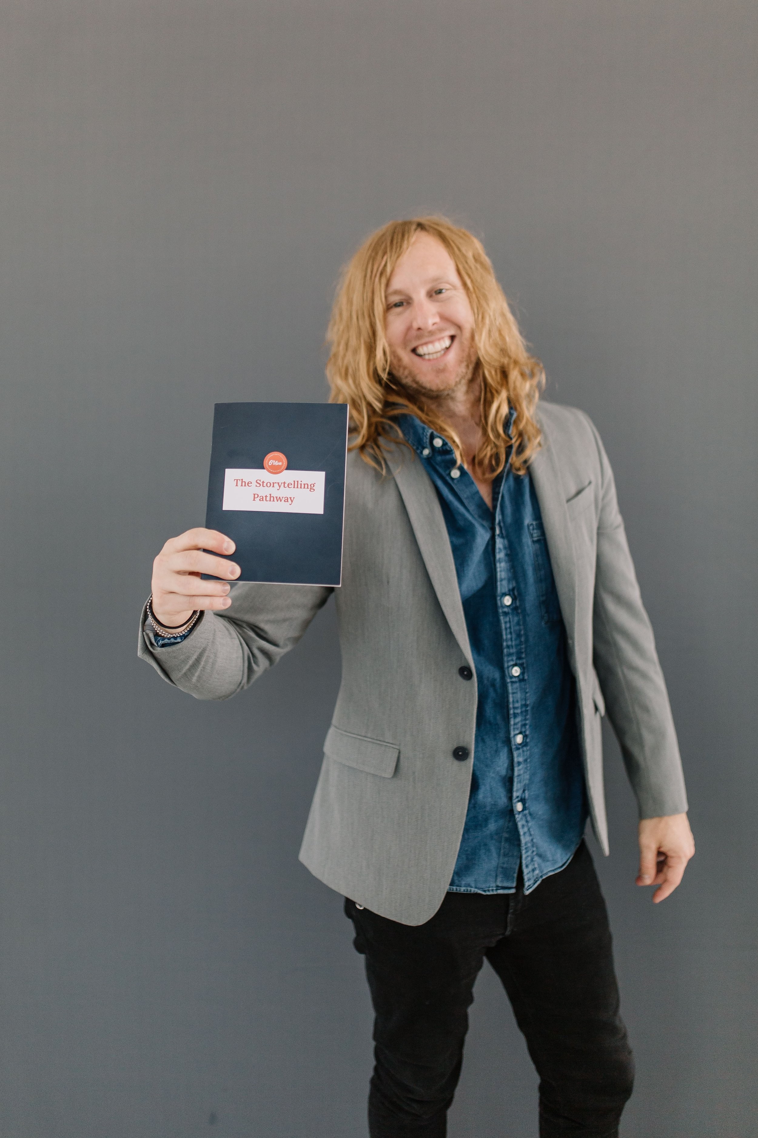 Jamey Ice holding up a small book against a grey wall.