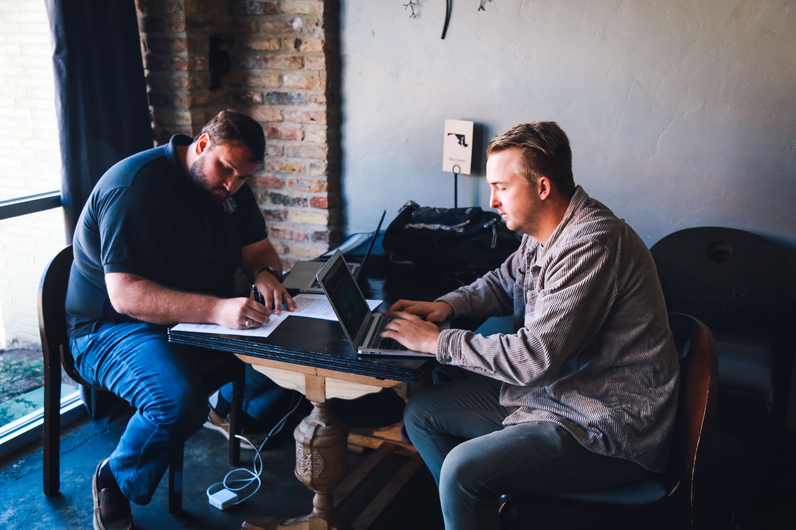 Two of Jamey Ice's early team at a table in Brewed, one writing on paper, one on a laptop.