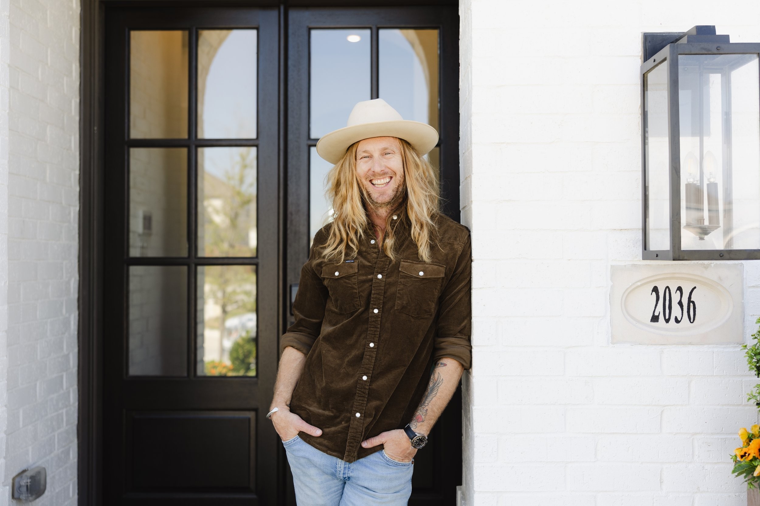 Jamey Ice smiling in the front doorway of a white brick house.