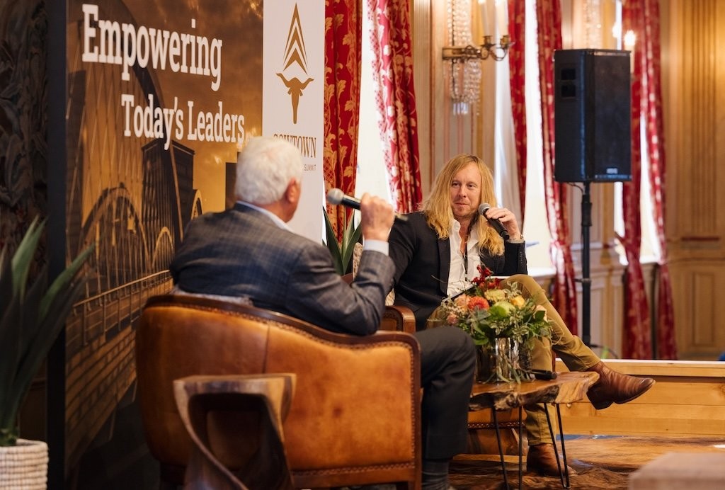 Jamey Ice on a stage in a fireside conversation with a business leader, a summit banner behind them.