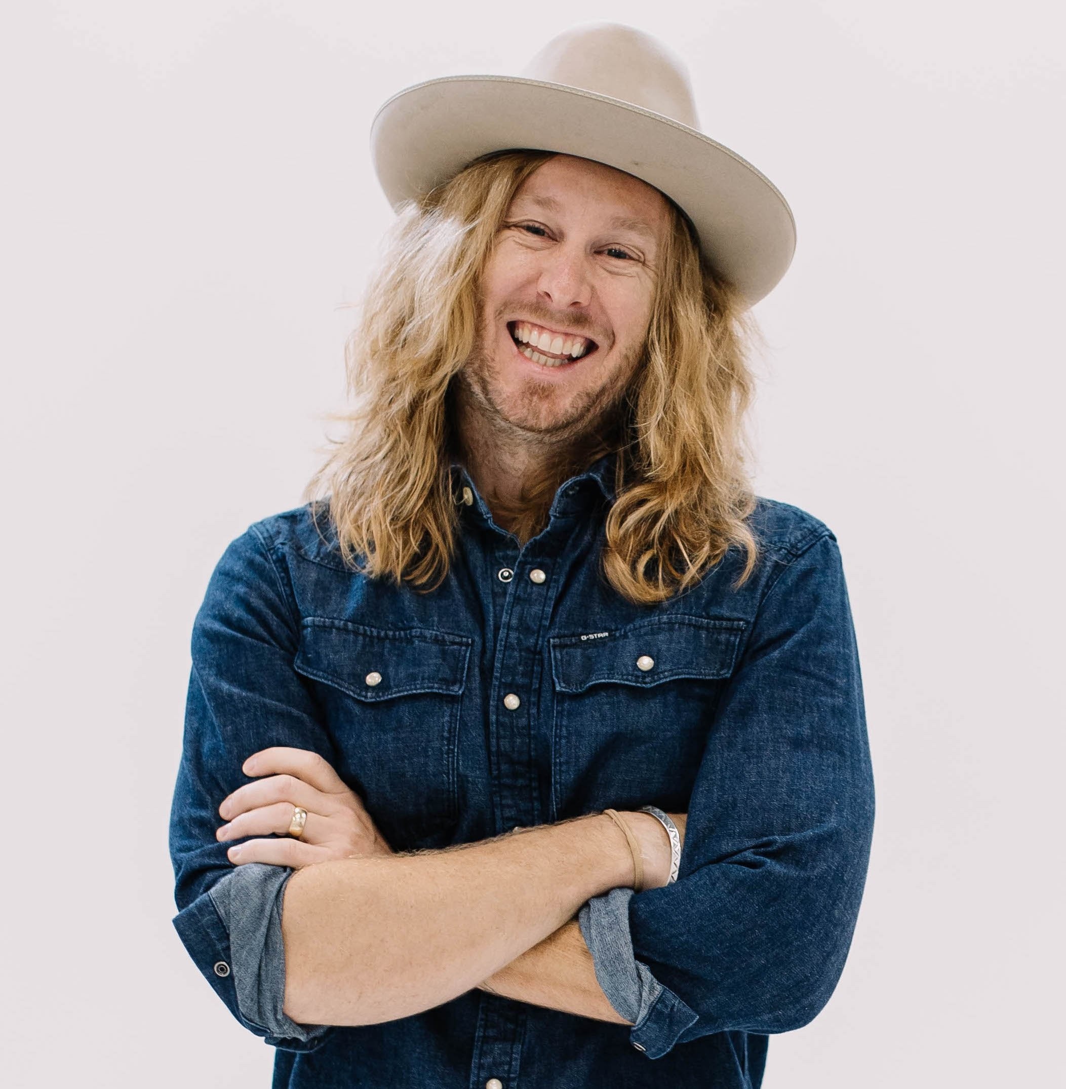 Jamey Ice in a denim shirt and hat, arms crossed, laughing.