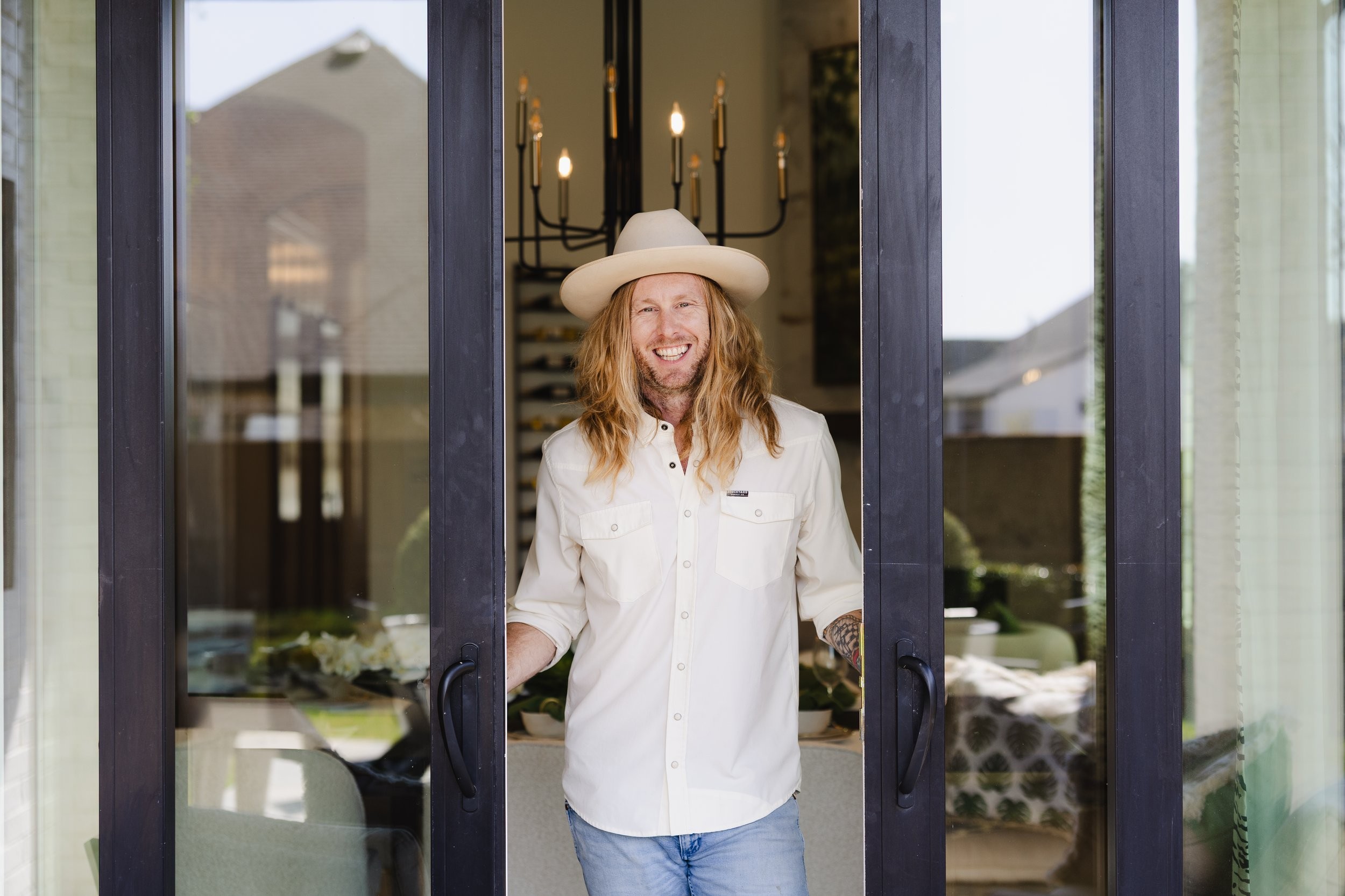 Jamey Ice smiling in an open glass doorway, in a white shirt and hat.
