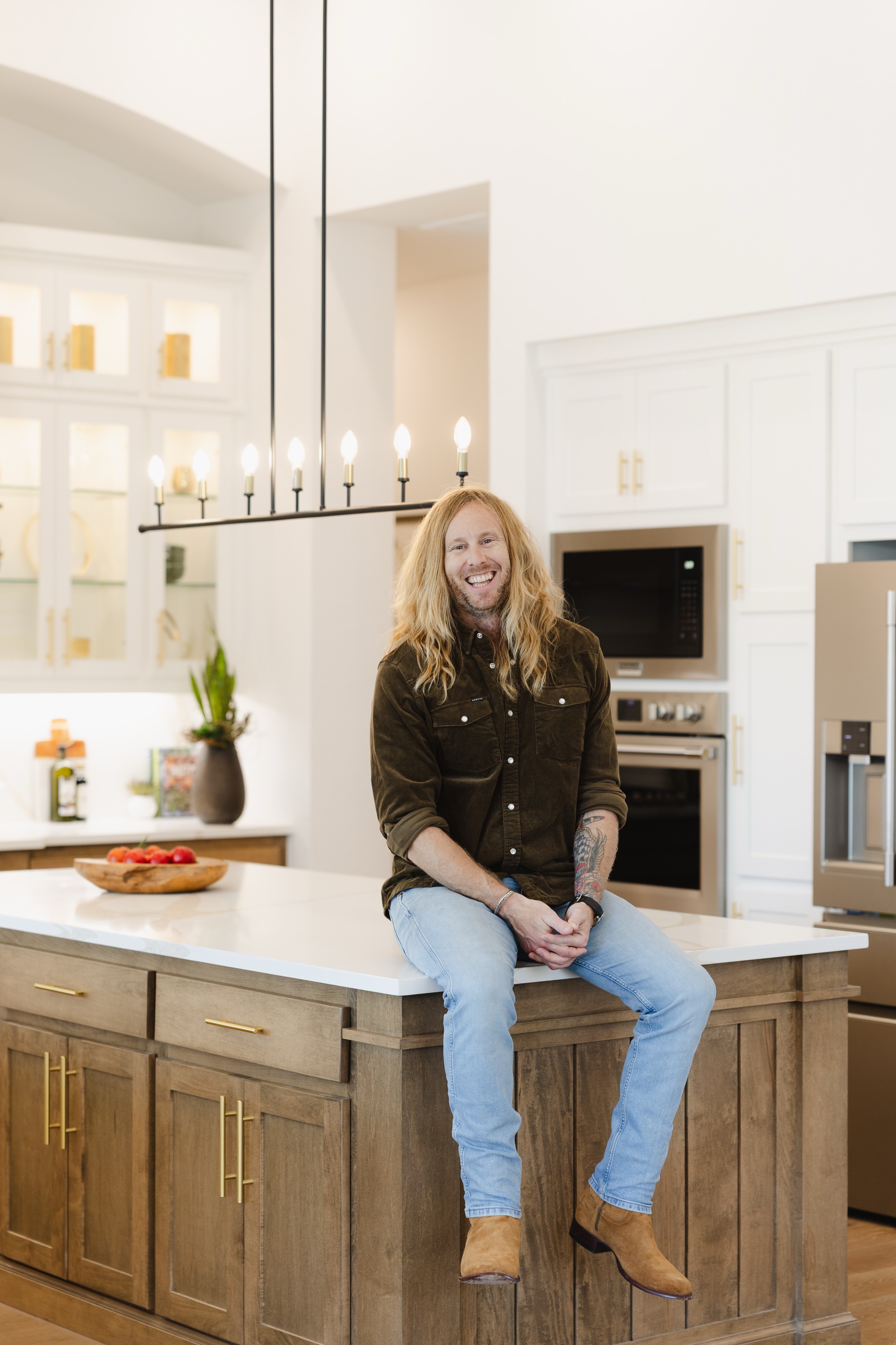 Jamey Ice laughing, sitting on a kitchen island with his hands clasped.