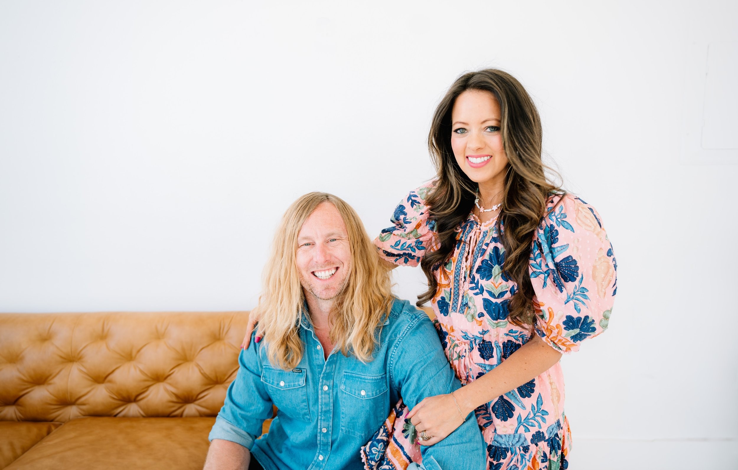 Melissa Ice leaning over Jamey on a leather sofa, both laughing