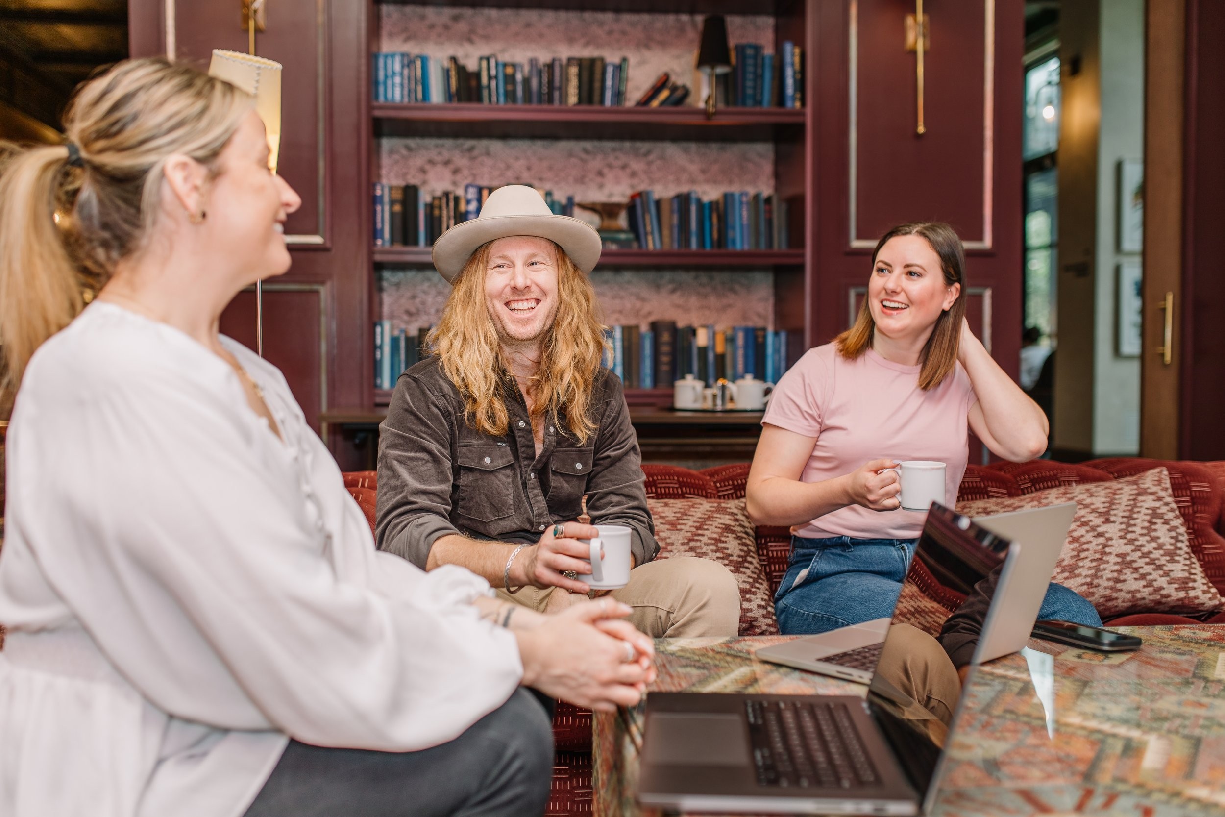 Jamey Ice laughing with two members of his team, laptops and coffee on the table.