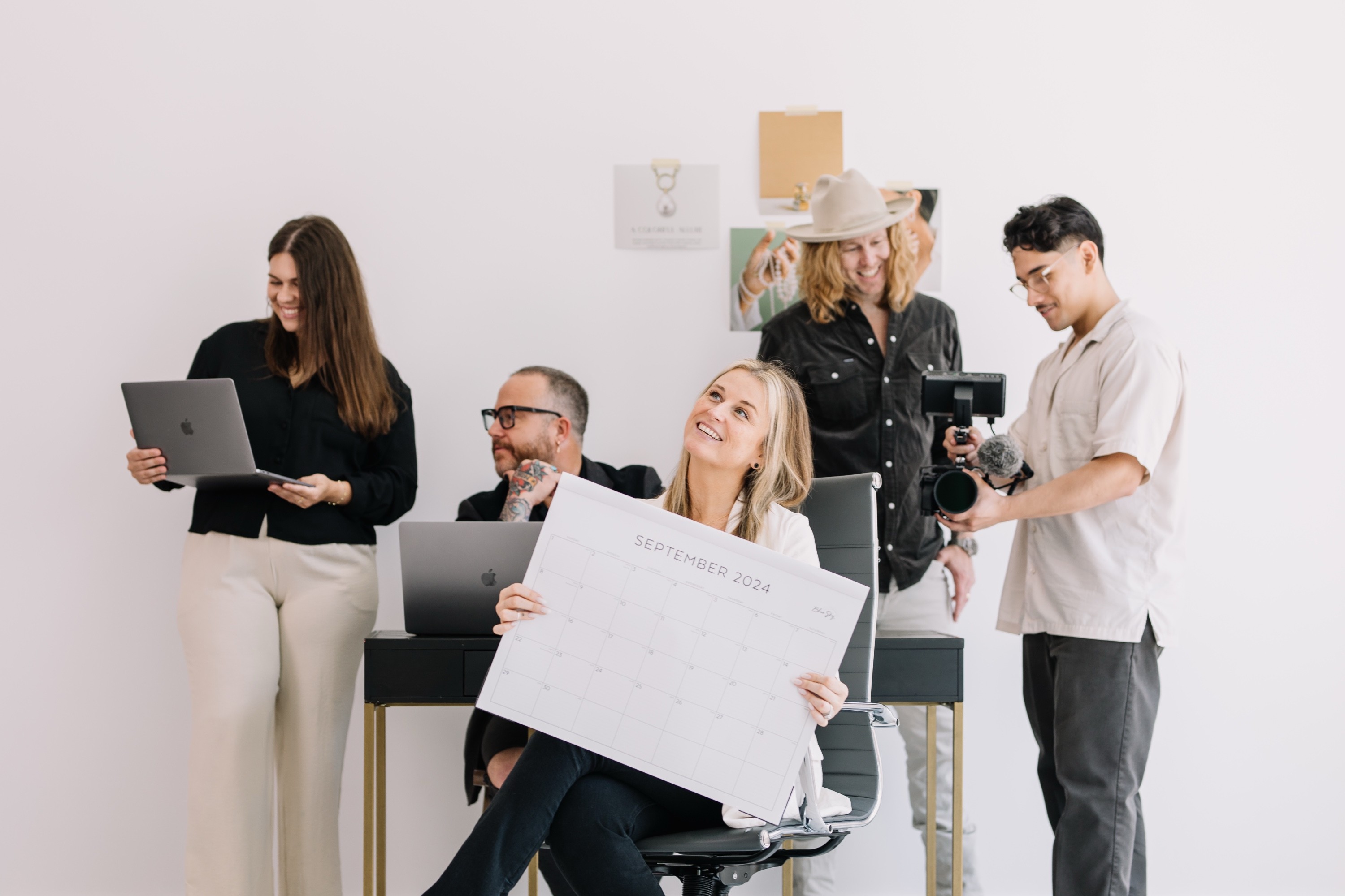 Jamey Ice in the middle of his agency's team at a 2024 shoot, a laptop, a video camera and the month's content calendar held up front.